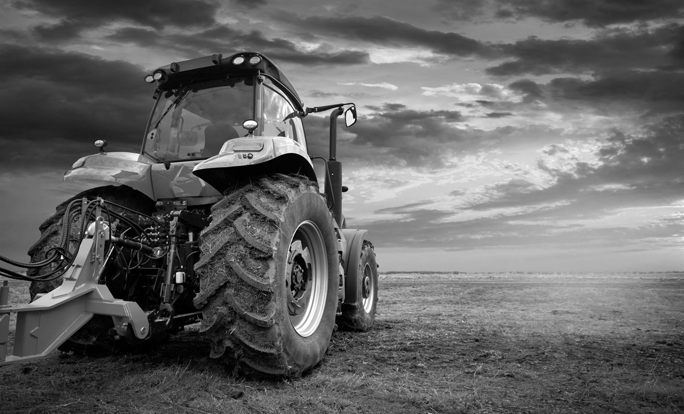Traktor auf einem Feld unter dramatischem Wolkenhimmel, schwarz-weiß